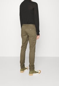 Olivové chinos kalhoty se slim fit, vyrobené z bavlněné směsi, s dvěma zadními kapsami, doplněné o zeleno-bílé tenisky.