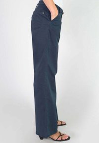 Marineblauwe, wijde broek van een lichtgewicht stof, met zijzakken en een hoge taille, gecombineerd met zwarte sandalen met straps.