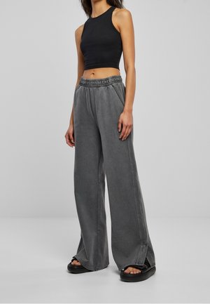 Szare szerokie spodnie z elastycznym paskiem w talii i bocznymi rozcięciami, zestawione z czarnym, krótkim topem bez rękawów oraz czarnym obuwiem. Gładka faktura.