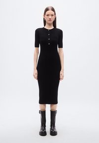 Μαύρο ριμπ midi φόρεμα με κοντά μανίκια, τρεις κουμπότρυπες και εφαρμοστή σιλουέτα, συνδυασμένο με γυαλιστερές μαύρες μπότες μέχρι το γόνατο.