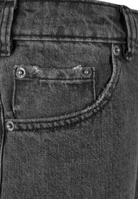 Jeans de denim negro con un bolsillo trasero con bordes desgastados, botones de metal y detalles de costura intrincados. La textura está ligeramente desgastada.