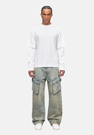 Witte korte mouwen gelaagde t-shirt gecombineerd met lichtblauwe baggy cargo jeans met grote zakken en een textuurafwerking, gedragen met witte sneakers.