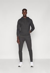 Felpa con cappuccio grigia scura e pantaloni jogger abbinati realizzati in morbido tessuto, con tasca a marsupio e dettagli con logo. Il modello indossa sneakers bianche.