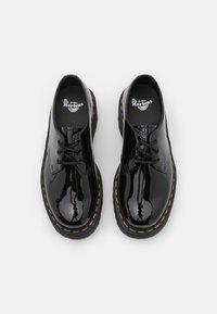 Scarpe in vernice nera con punta rotonda, design con lacci, cuciture gialle lungo la suola e soletta imbottita.