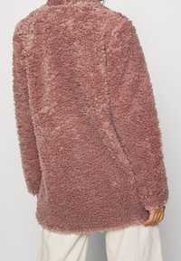 Rosa plysjakke med en tekstureret, fluffy overflade, lange ærmer og en løs pasform, med et enkelt design og høj krave.