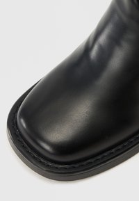 Bottine en cuir noir avec une texture lisse, un bout rond et un contraste de couture le long du bord de la semelle.