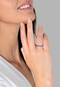 Silberner Bandring mit lila Edelsteinen, glatte polierte Oberfläche, rechteckige Form, getragen an einer Hand in der Nähe des Gesichts vor einem neutralen Hintergrund.