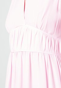 Robe rose clair avec un décolleté en V, texture froncée à la taille et jupes fluides. Tissu doux et léger avec une finition lisse.