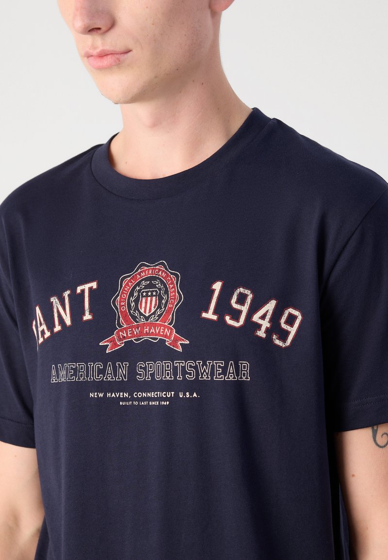 Granatowa bawełniana koszulka z okrągłym dekoltem, z graficznym logo zawierającym tekst "1949" oraz "AMERICAN SPORTSWEAR" w kolorach czerwonym i białym.