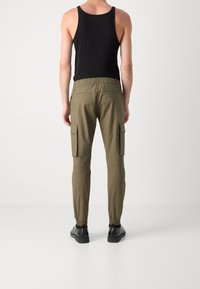 Pantalon cargo kaki avec taille élastique, jambes fuselées, poches latérales et poches arrière ; associé à un haut noir sans manches et des chaussures.