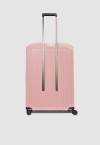 Valigia rigida rosa con coste verticali, doppio manico trolley in metallo e quattro ruote nere per la mobilità. Texture liscia e design robusto.