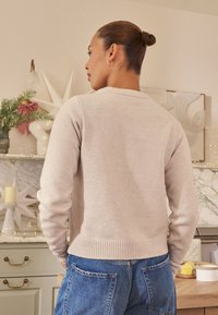 Jasnoszary sweter dzianinowy z prążkowanym wykończeniem na dole i przy mankietach, zestawiony z niebieskimi dżinsami. Miękka faktura, casualowy design i luźny krój.