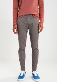 Grå bomullsbyxor med slim fit, framfickor och knappstängning. Kombination med blå sneakers och en rostfärgad långärmad skjorta.