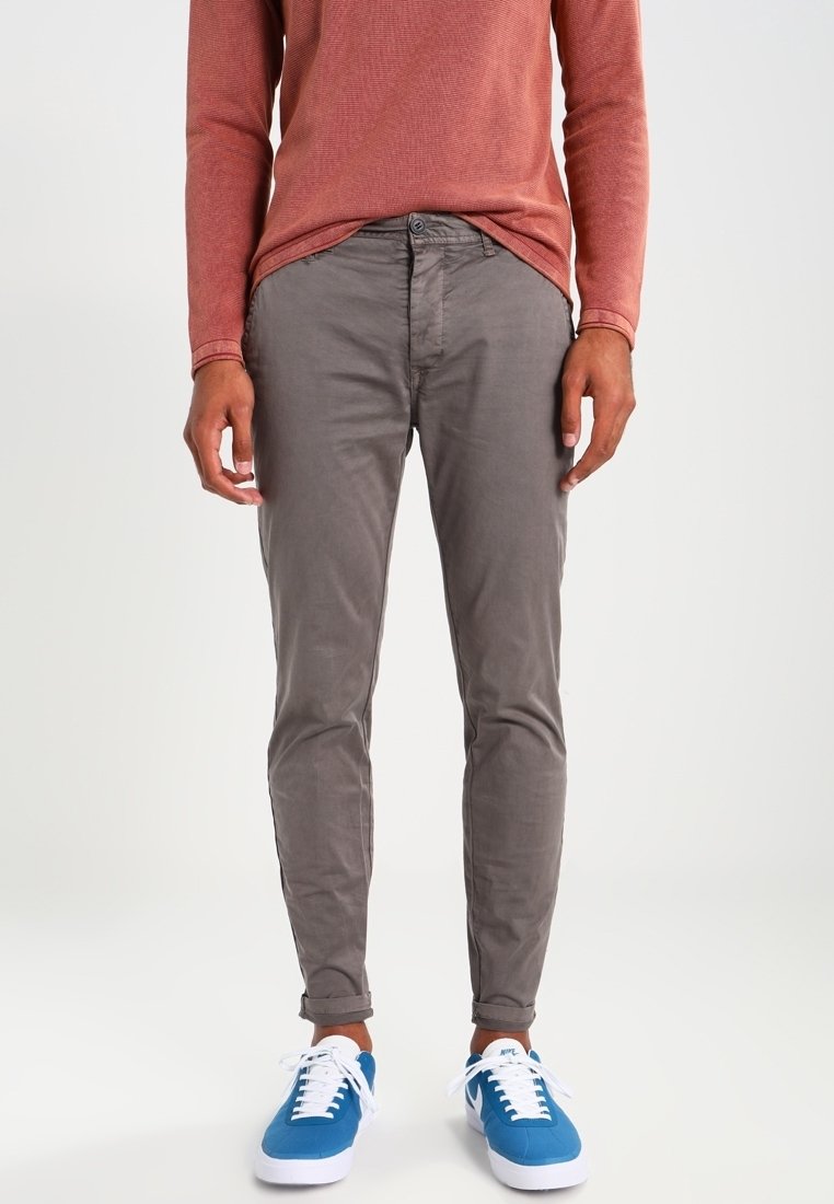 Grå bomullsbyxor med slim fit, framfickor och knappstängning. Kombination med blå sneakers och en rostfärgad långärmad skjorta.