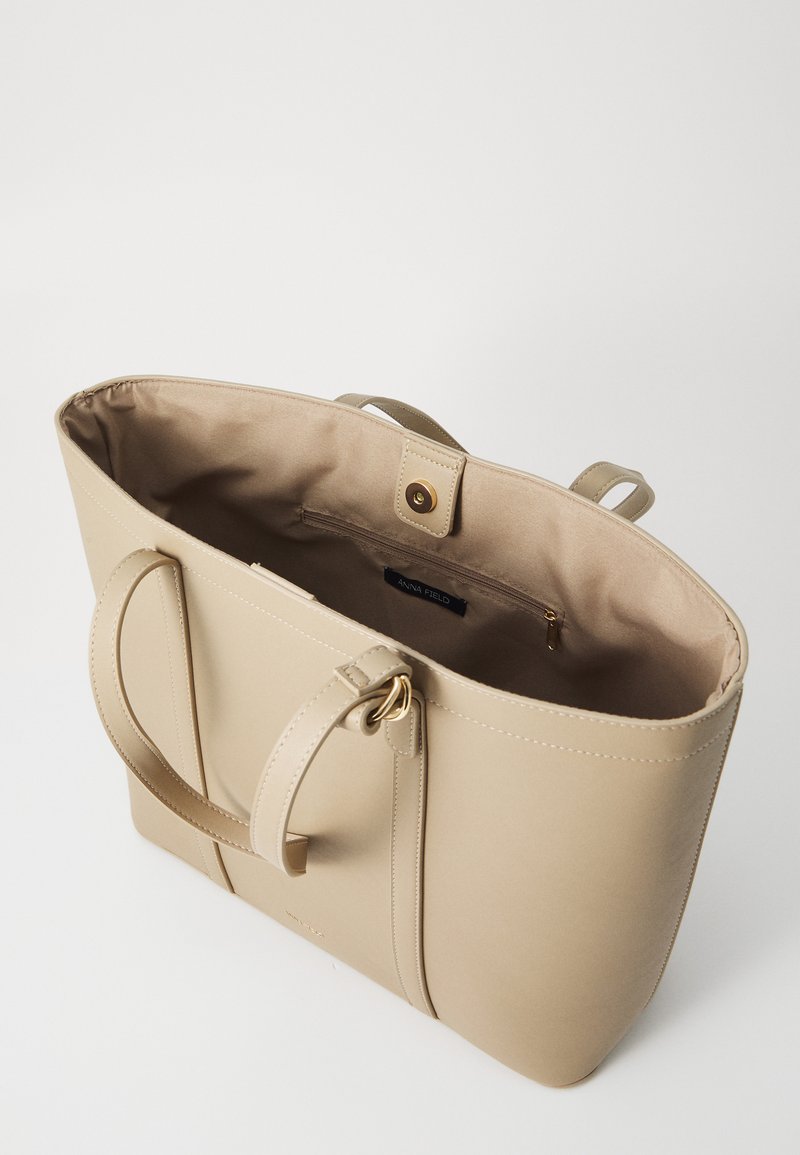 Bolso tote de piel sintética beige con textura suave, doble asa y cierre de imán. El interior cuenta con un bolsillo con cremallera.