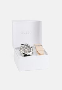 Reloj cronógrafo plateado con correa de silicona negra y una segunda correa intercambiable en tono sonrojado, presentado en una caja blanca.