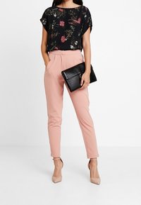 Černá květinová blůza s krátkým rukávem, růžové kalhoty na míru a černá texturovaná kabelka. Celý vzhled doplňují nahé vysoké podpatky.