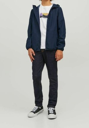 Marineblå let zip-up jakke med hætte, hvid grafisk t-shirt, mørke denim jeans og sort-hvide sneakers. Afslappet outfit.