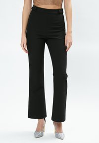 Zwarte, high-waisted broeken met een getailleerde pasvorm, voorzien van dubbele knopen op de taille en een uitlopende broekspijp. Gladde textuur.
