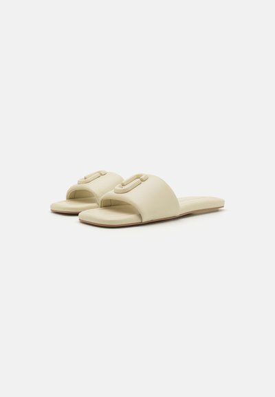Light beige slide sandals with a wide strap and a prominent decorative buckle. Flat sole, smooth texture, minimalistic design.
