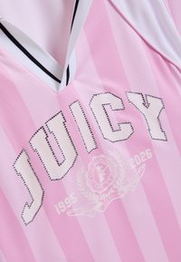 Ροζ και λευκή ριγέ αθλητική φανέλα με τη λέξη «JUICY» σε στρασάκια, ένα έμβλημα με κρεσέντο και τις χρονιές 1995 και 2026 στο μπροστινό μέρος.