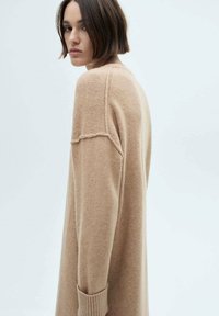 Beige oversized tröja med en mjuk textur, sänkt axlar och ribbade muddars, med en avslappnad silhuett och minimala sömmar.