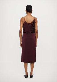 Rochie din satin burgundy cu bretel cu ajustare, spate drapat și o siluetă de lungime medie, având o textură moale și netedă.
