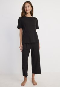 Czarny zestaw wypoczynkowy składający się z bluzki z krótkim rękawem z kieszenią na piersi oraz spodni z szerokimi nogawkami. Miękki materiał, luźny krój i długość do kostek.