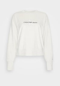 Bílá zkrácená mikina vyrobená z měkké tkaniny, zdobená vyšívaným logem "Calvin Klein Jeans" a "K" na rukávu. Kulatý výstřih a dlouhé rukávy.