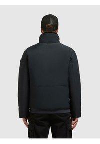 Czarna pikowana kurtka z wysokim kołnierzem, gładkim wierzchnim materiałem i widocznym przeszyciem. Posiada boczne kieszenie oraz naszywkę z logo na plecach.