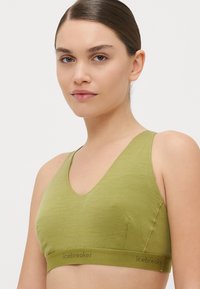 Bralette verde oliva com design em V, textura sem costuras e uma banda larga com o logótipo "icebreaker". Tecido macio e elástico.