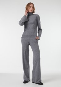 Grijze gebreide coltrui met lange mouwen en ribgebreide accenten, gecombineerd met bijpassende grijze wijde broek, gemaakt van zacht materiaal.