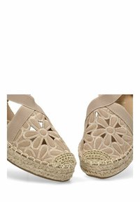Zapatos de esparto beige con patrón floral troquelado, correas elásticas y suela de yute trenzado. Parte superior de tela texturizada y diseño de punta redonda.