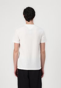Tricou alb cu mânecă scurtă, fabricat dintr-un material moale cu o textură netedă. Prezintă un design simplu și un mic detaliu în formă de V la spate.