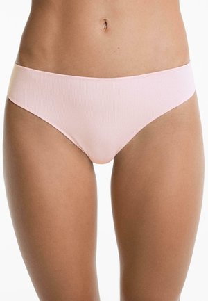 Vrouw in lichtroze ribbed bikini-ondergoed, die haar middengedeelte en bovenbenen toont tegen een witte achtergrond.