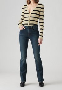 Ribbad, långärmad cardigan i cream med svarta ränder; kombinerad med mörk tvätt, utsvängda jeans och svarta ankelboots.