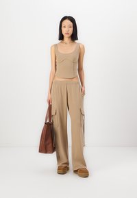 Top de tirantes ajustado beige con escote redondeado, combinado con pantalones cargo de pierna ancha beige con bolsillos laterales. Bolso de mano marrón y zapatos gruesos.