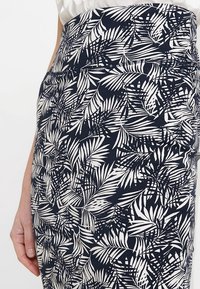 Gros plan d'une personne portant une jupe taille haute avec un motif de feuilles tropicales noir et blanc, la main reposant sur le côté.