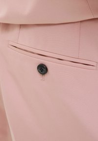 Ružičaste tkanine hlače s glatkom teksturom, s horizontalnom džepom i crnim dugmetom kao detaljem sa strane.