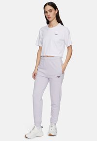 Maglietta bianca cropped con logo nero e pantaloni jogger viola chiaro. I jogger presentano una vita elasticizzata, tasche laterali e polsini a coste.