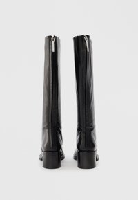Stivali neri in pelle al ginocchio con una superficie liscia, cerniere laterali e tacco spesso, che mostrano un design minimalista e una silhouette elegante.