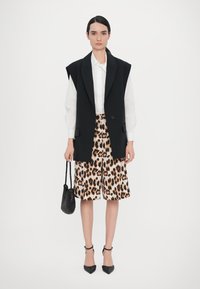 Black oversized blazer, white shirt, beige leopard print shorts, black ankle strap heels, and a textured black handbag.