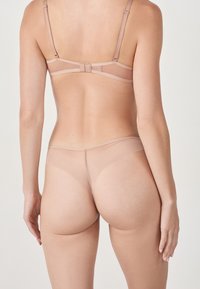 Ensemble de lingerie beige comprenant un soutien-gorge transparent avec des bretelles ajustables et un string assorti, texture lisse et design minimaliste.