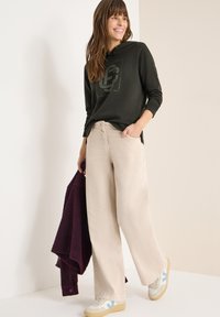 Ciemnozielona bluza z kapturem z nadrukiem, beżowe spodnie o szerokich nogawkach, jasne buty sportowe z niebieskimi akcentami oraz teksturowany bordowy sweter.