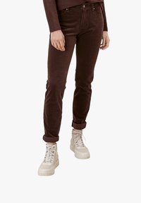 Pantalones de pana marrones de corte ajustado, con los puños enrollados, combinados con zapatillas altas de color beige claro que cuentan con suelas texturizadas y acentos metálicos.
