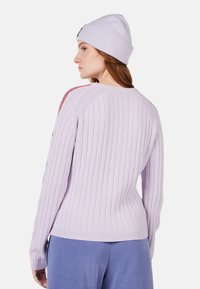 Helles lavendelfarbenes, geripptes Sweatshirt mit langen Ärmeln, das einen strukturierten Stoff zeigt. Kombiniert mit einer passenden helllila Strickmütze.