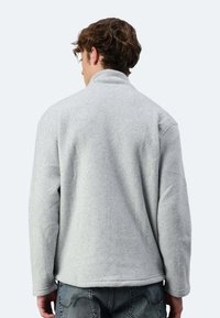 Giacca in pile grigia con colletto alto, maniche lunghe e vestibilità rilassata, caratterizzata da una superficie testurizzata e spalle senza cuciture.