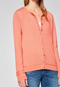 Korálový svetřík z jemného pleteného materiálu, s kulatým výstřihem, zapínáním na knoflíky a dlouhými rukávy. Má žebrované manžety a lem.