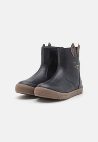 Botas de cuero negras hasta el tobillo con un acabado suave, suela de goma marrón y orejas decorativas con un patrón de leopardo y rasgos faciales cosidos.