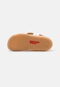 Brun gummisula med en texturerad yta och en röd märkesdetalj. Designen �är platt med en rundad form, lämplig för avslappnad användning.